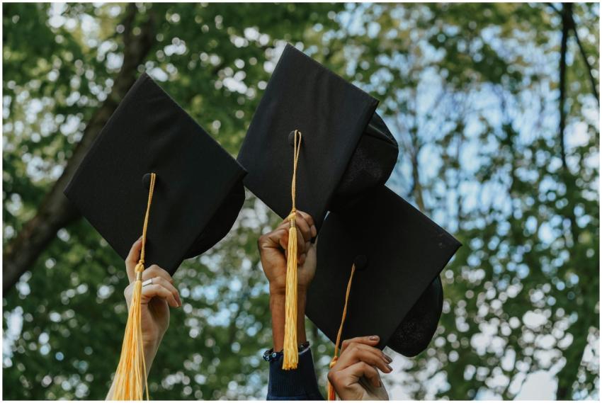 Three hands holding graduation caps in celebration