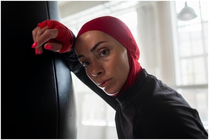 Muslim woman boxer in hijab resting on punching ba