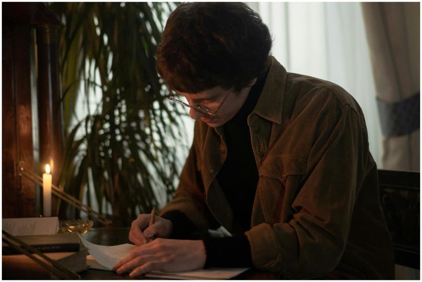 A person in glasses writing at a desk by candlelig