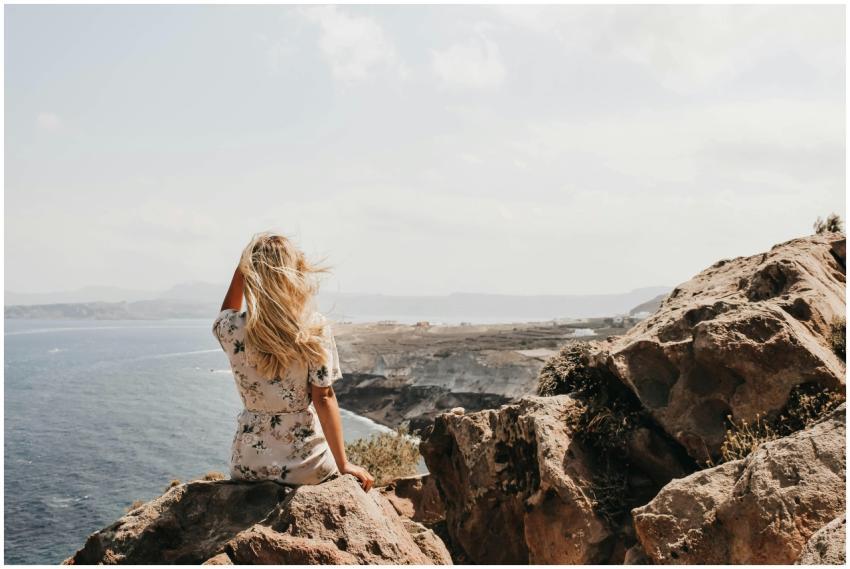 A woman with blonde hair sits on a rocky cliff in