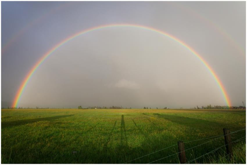 A full rainbow arches over a serene farmland lands