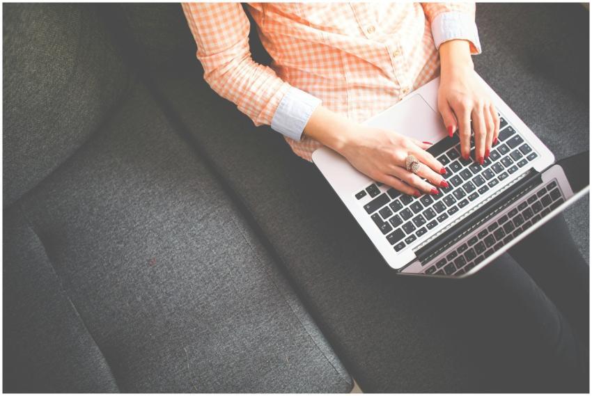 A woman typing on a laptop, sitting on a sofa in c