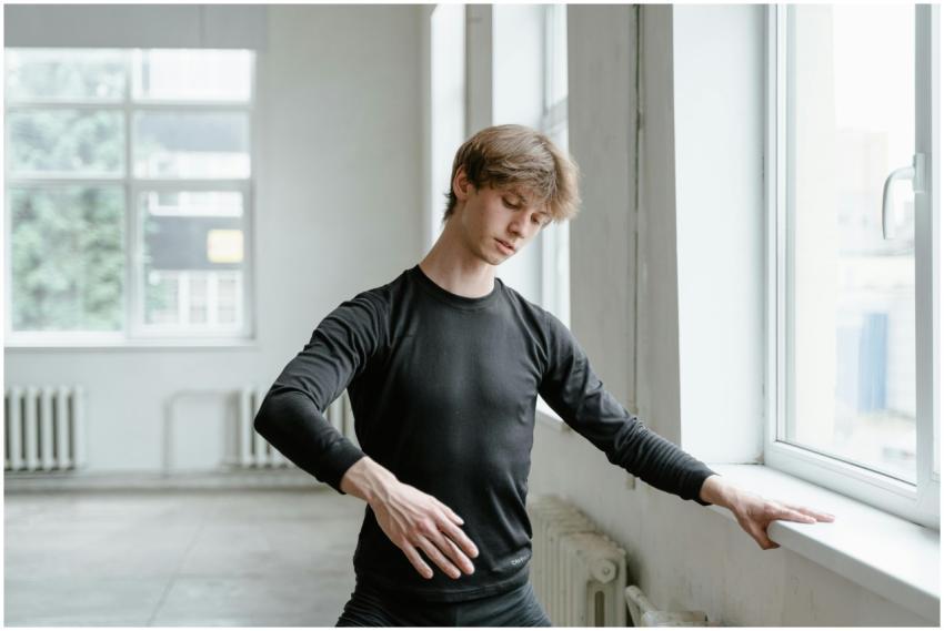 A young male ballet dancer practicing near a windo