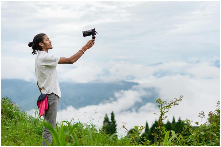 A young man films a lush, misty mountain landscape