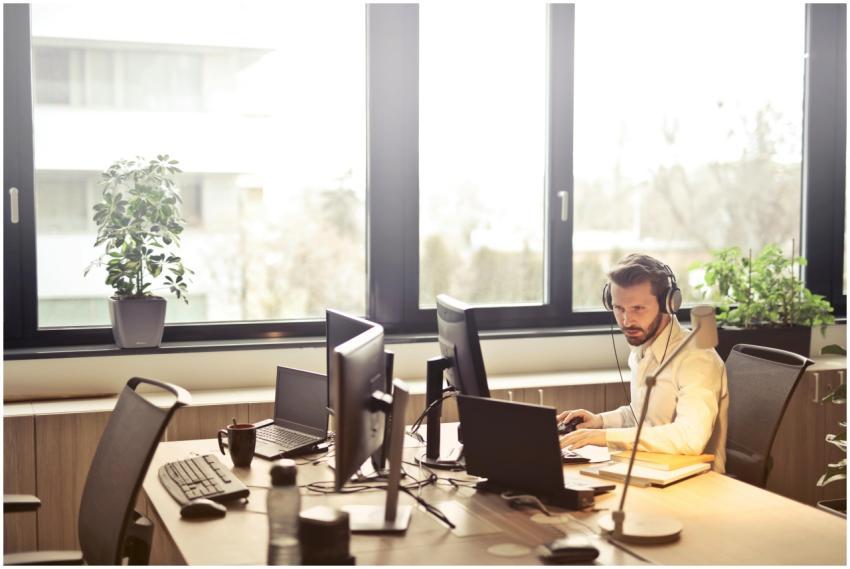 A businessman sits at a desk using multiple comput