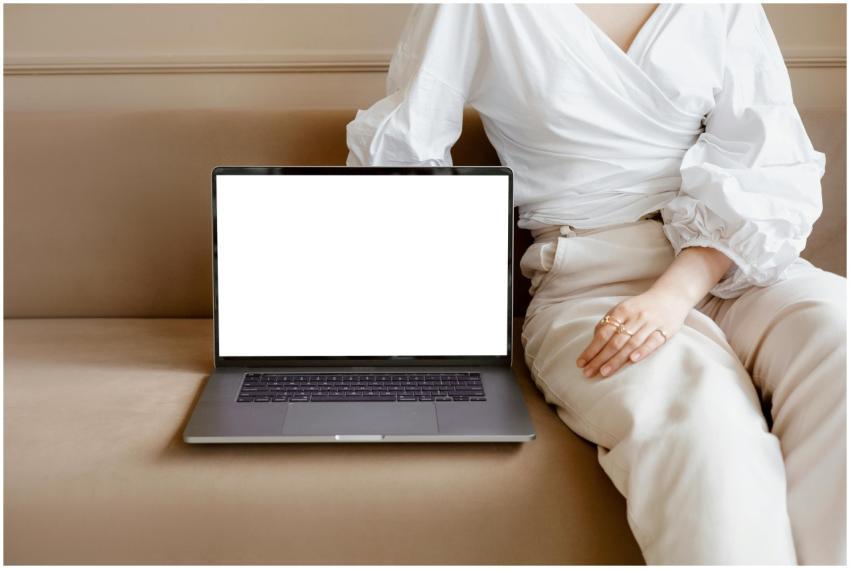 An adult sitting on a sofa with a blank laptop scr