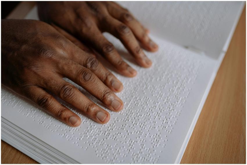 Close-up of hands reading Braille text on paper. E