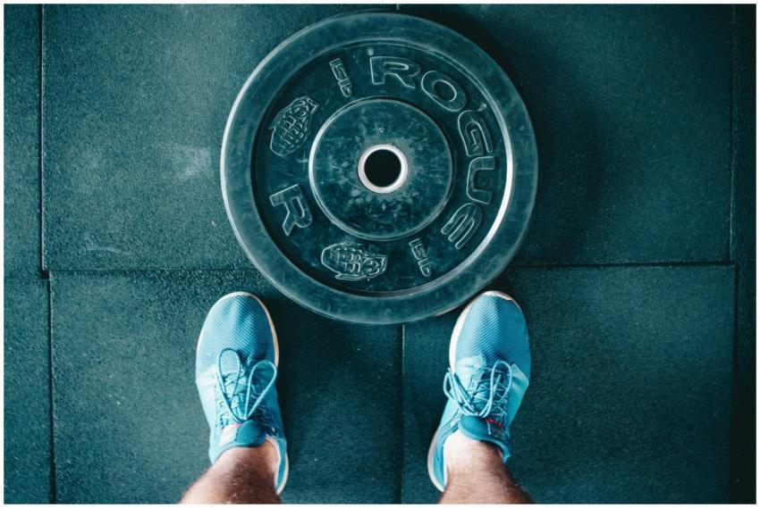 Blue sneakers next to a weight plate on a gym floo