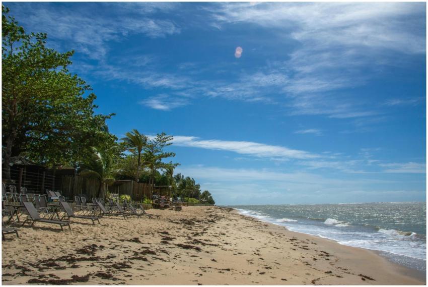 Empty beach chairs line a sandy shore under a brig
