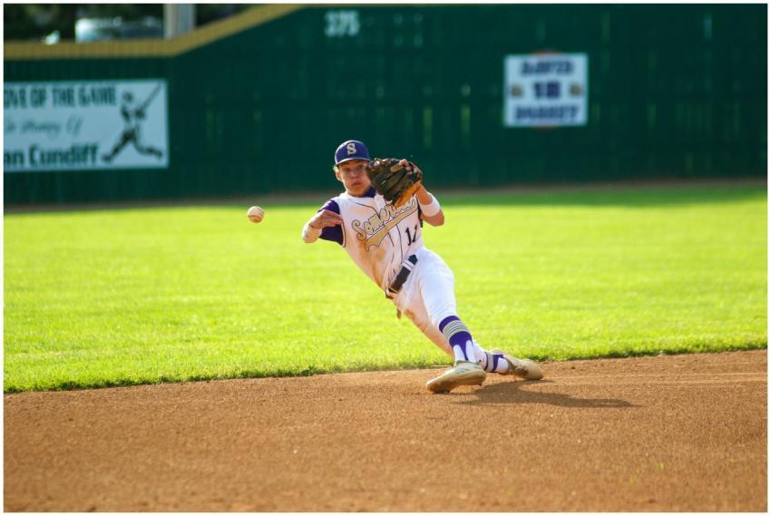 A young baseball player in uniform dives to catch