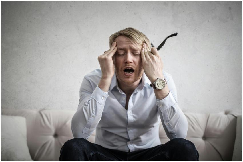 Stressed man sitting on couch, feeling overwhelmed