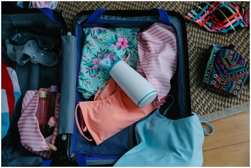 A packed suitcase with swimwear, goggles, and esse