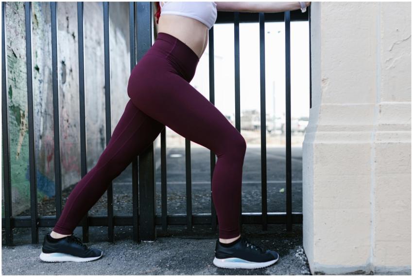 Woman stretching against a metal fence in athletic