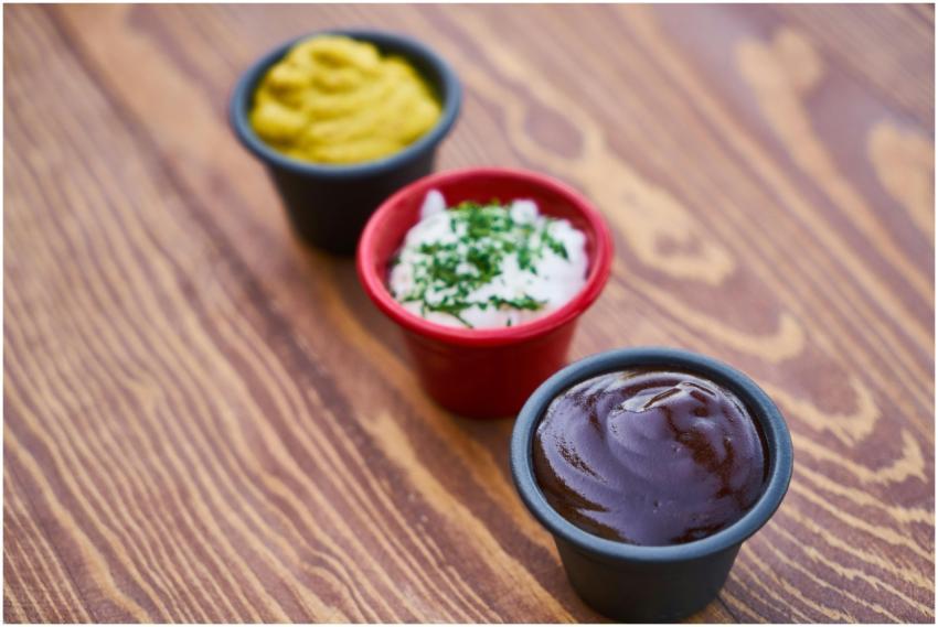 A close-up of three sauces in cups on a wooden sur