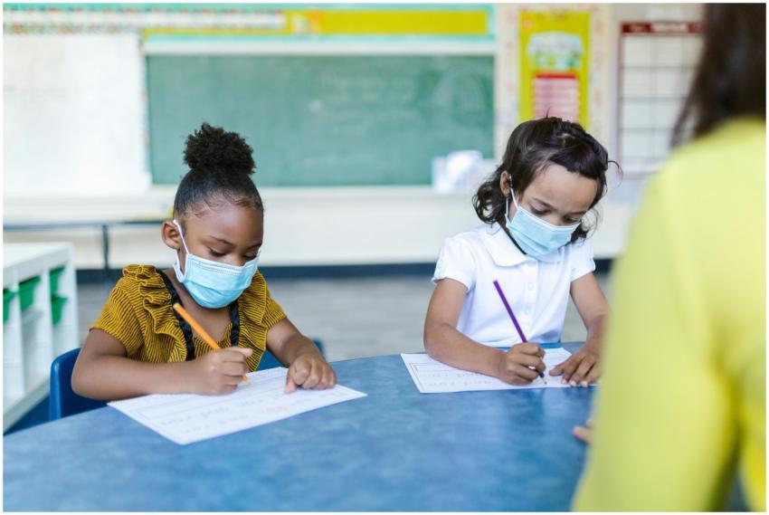 Young children in masks write in a classroom, focu