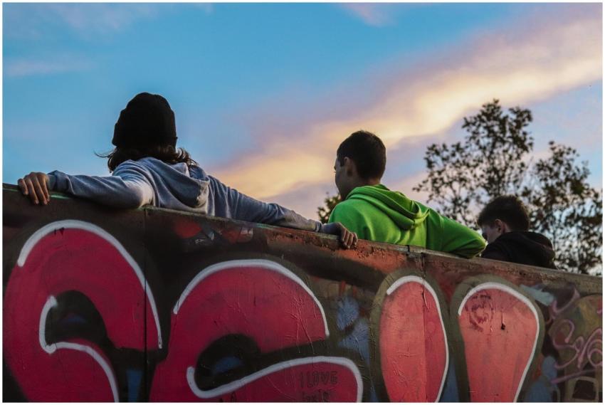 Three teenagers relax by a graffiti wall at sunset
