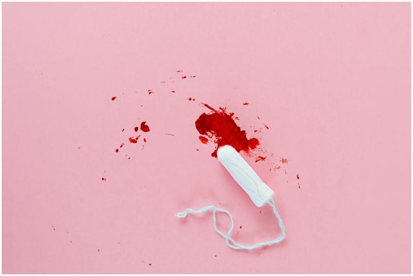 White tampon with red blood stain on pink surface.