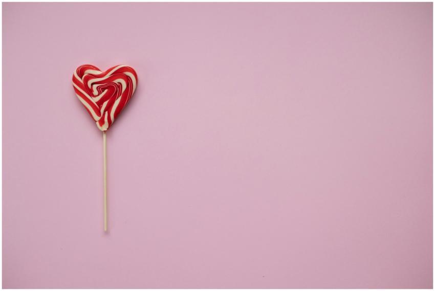 A heart-shaped red and white lollipop on a pink ba