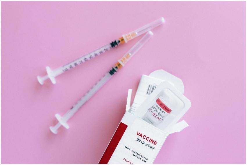 Close-up of vaccine vial and syringes on a pink ba
