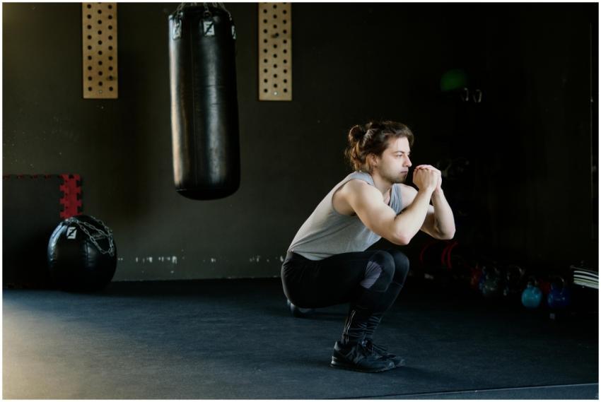 A man is doing squats in a gym with a punching bag