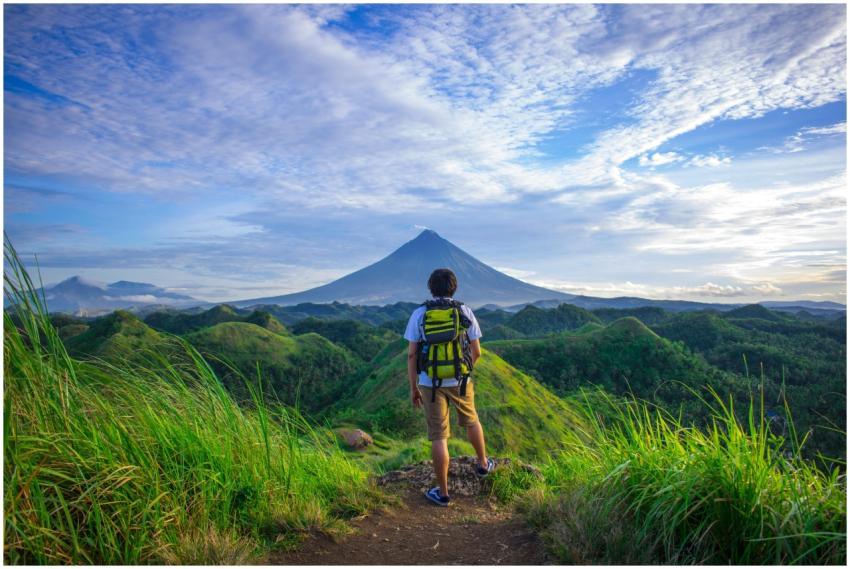 A hiker enjoys the scenic view of Mount Mayon in t