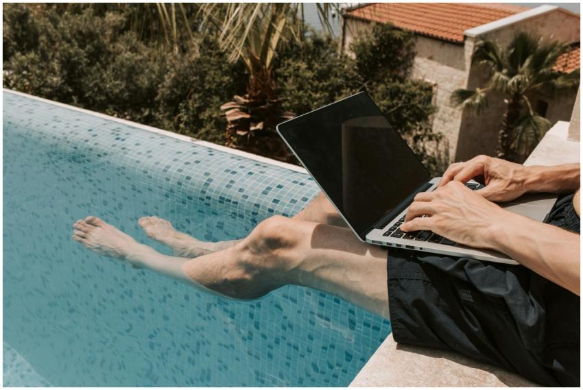Man working on a laptop while relaxing by a pool i