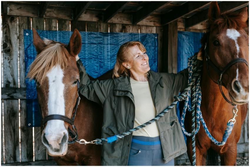 Smiling senior woman bonding with two horses in a