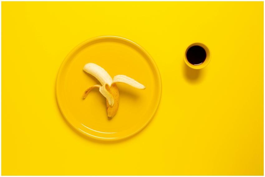 A peeled banana on a yellow plate beside a cup of