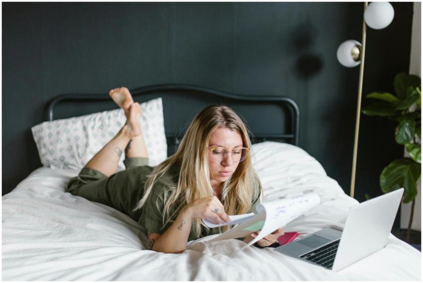 Young woman working from home, lying on bed with l