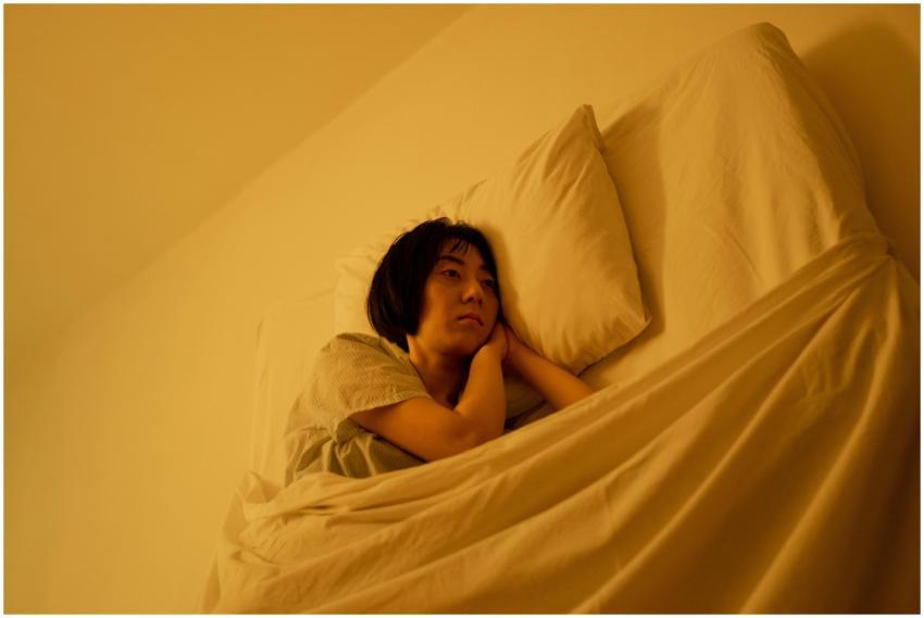 A woman in pajamas lies in bed, reflecting her emo