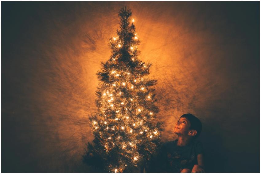 A child smiles at a beautifully lit Christmas tree