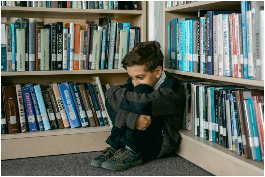 Young boy in library appears sad, sitting alone am