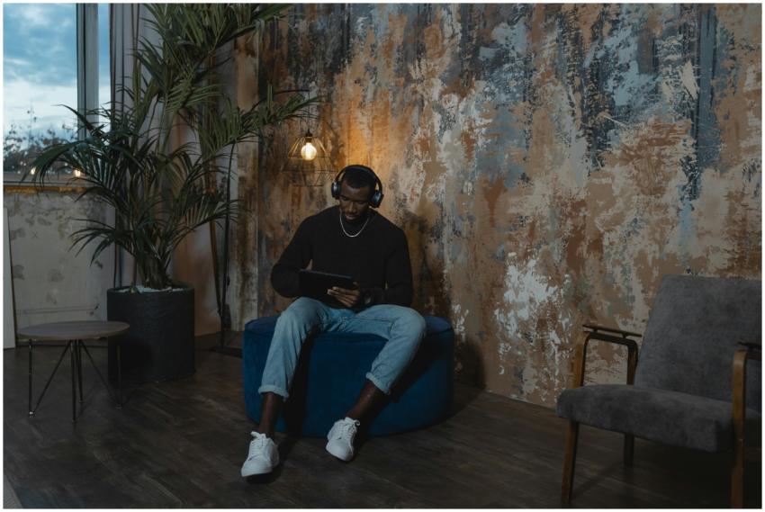 A man wearing headphones sits with a tablet in a s