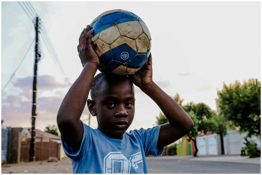 A young boy in a blue shirt holds a soccer ball on
