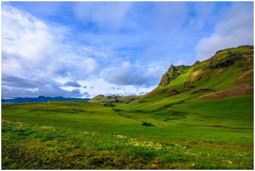 Expansive green valley under a bright blue sky wit