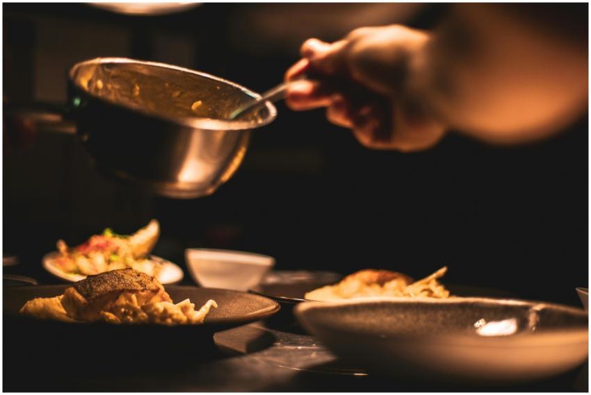Gourmet dish being plated by a chef in a dimly lit