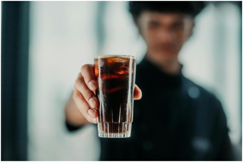 Close-up of a person offering a glass of dark beve
