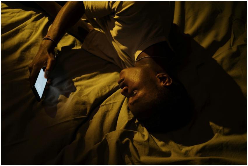 A man lying in bed at night, illuminated by a smar