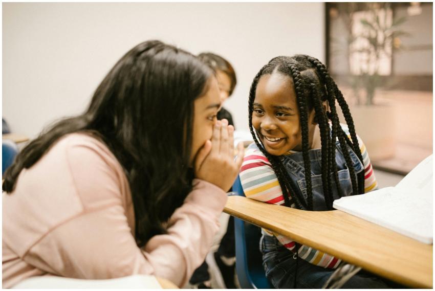 Two girls whisper and smile in a classroom, foster