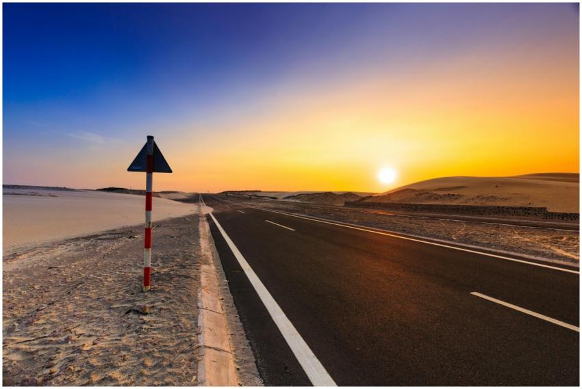 A scenic highway in a desert setting at sunset wit