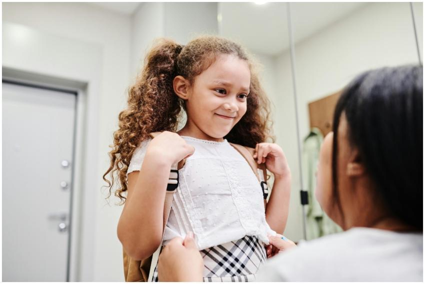 A smiling young girl with curly hair ready for sch