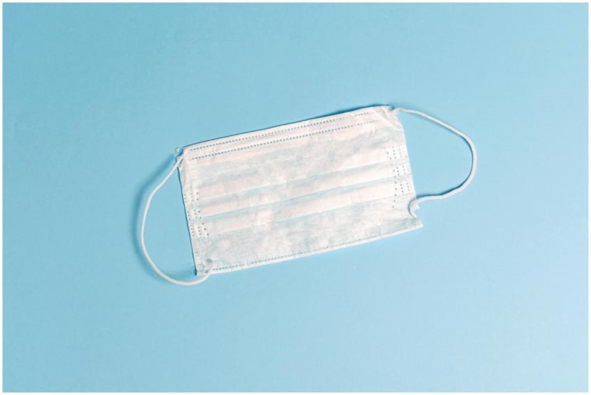 A disposable face mask lying on a light blue surfa