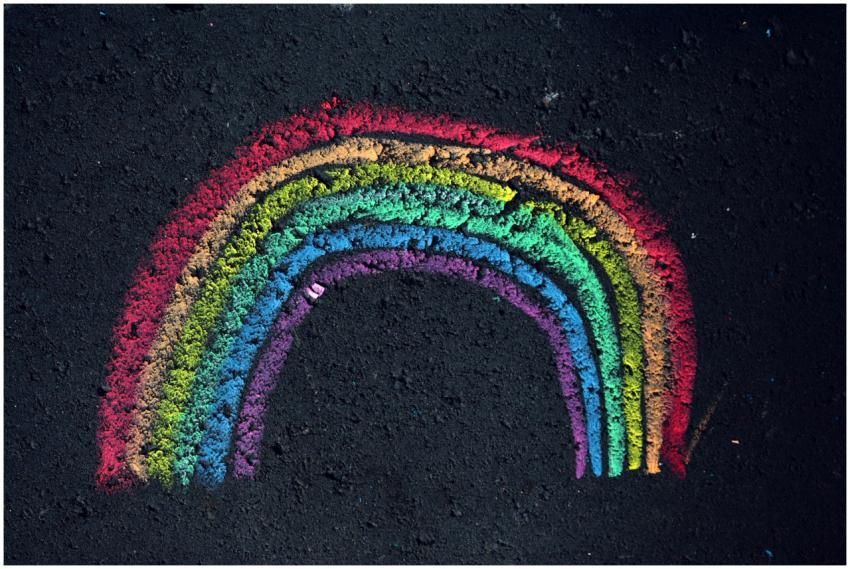 Colorful chalk rainbow drawn on dark pavement, sho