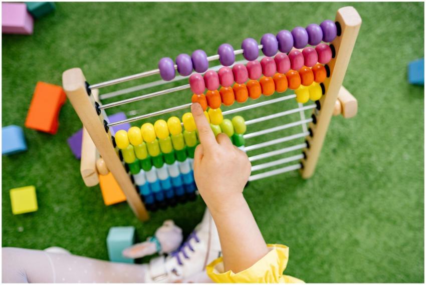 A child's hand using a colorful wooden abacus on g