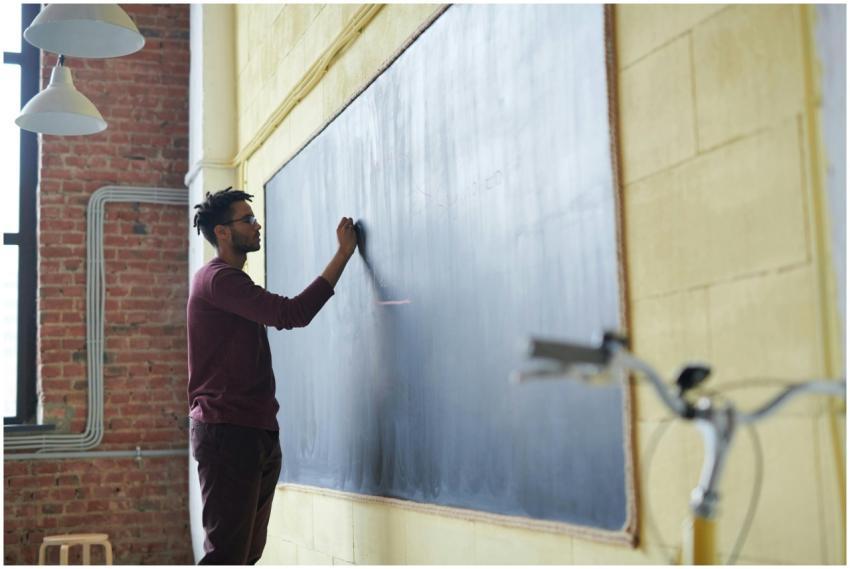 Man with dreadlocks writing on a blackboard in a c