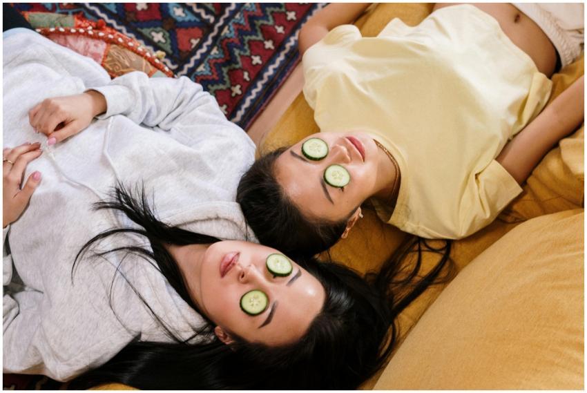 Two friends relaxing at home with cucumber masks i