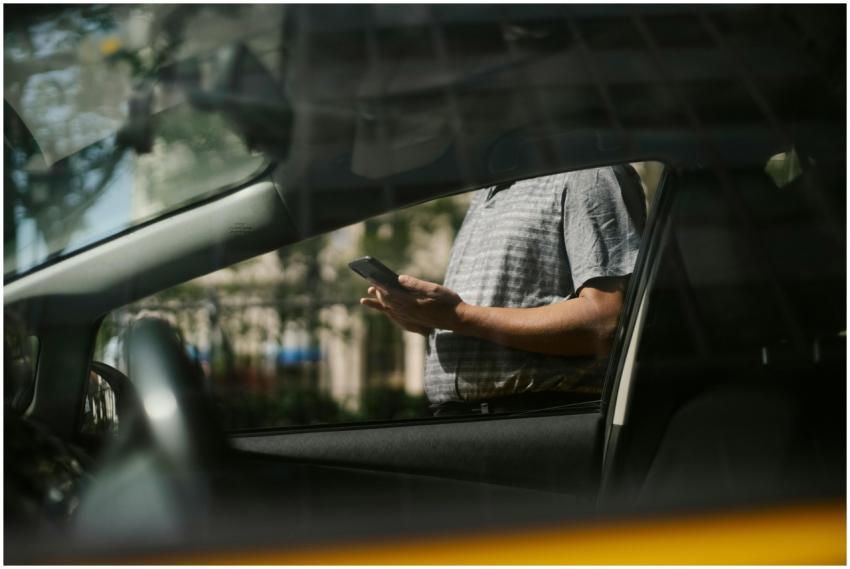 A man using a smartphone inside a car, visible thr