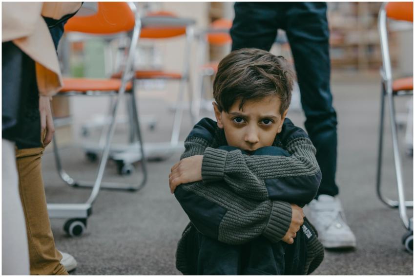 A young boy sits on the floor of a classroom, expr