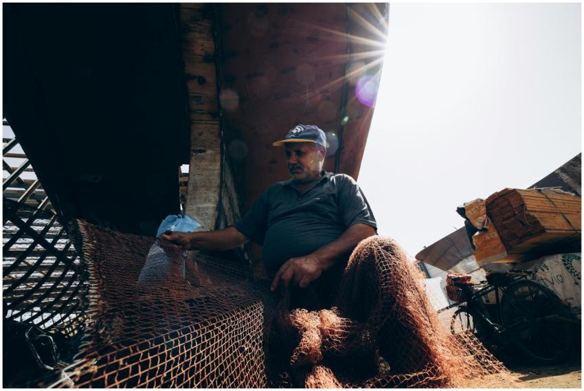 A fisherman mends a net under bright sunlight in D
