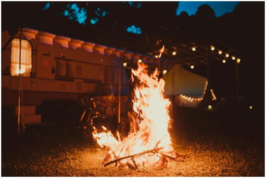 A warm campfire lighting up the night beside a car